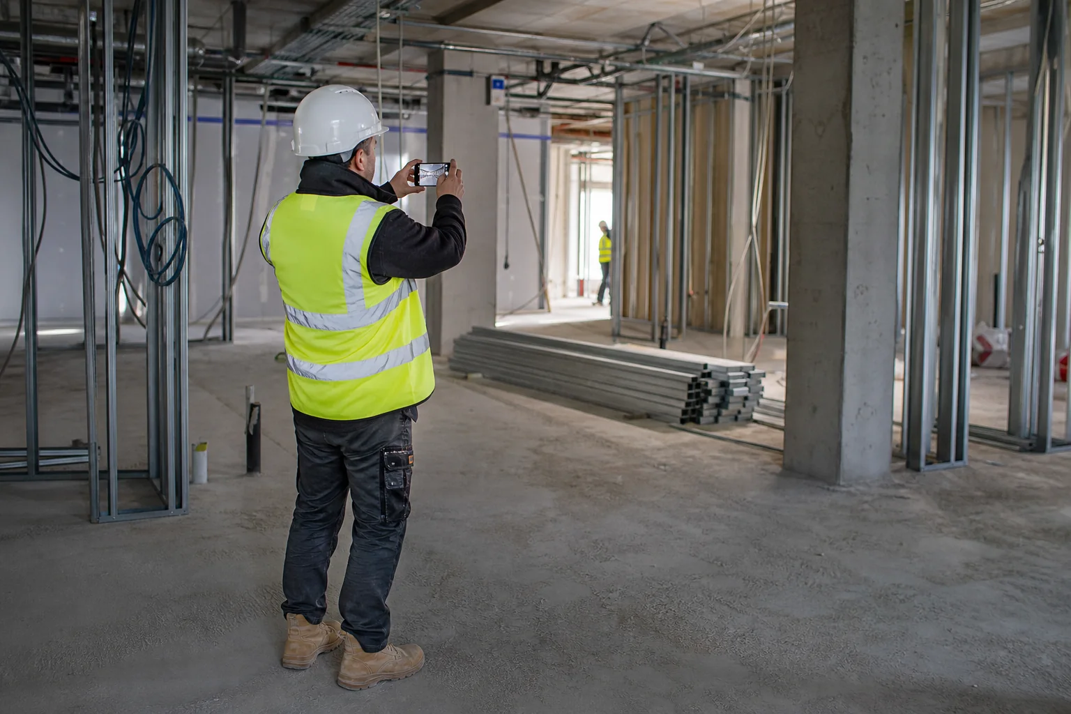 Chef de chantier photographiant l'avancement des installations et des cloisons intérieures depuis une zone sûre